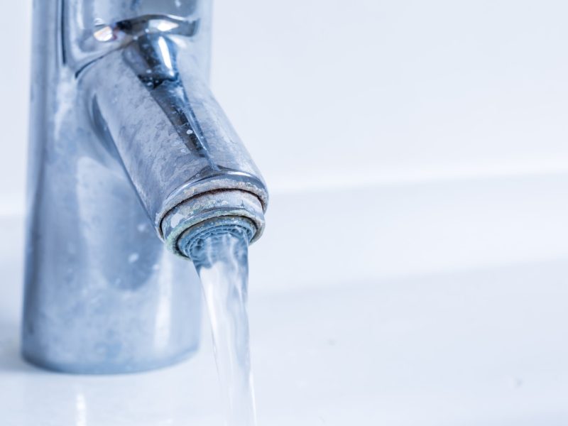 Faucet flowing water and with limescale. Detail of dirty and calcified bathroom taps before descaling.